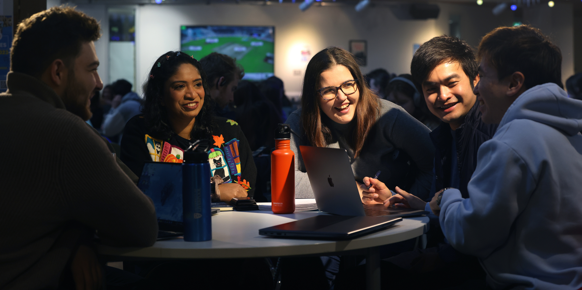 Students laughing and chatting in the students union at a table with a laptop